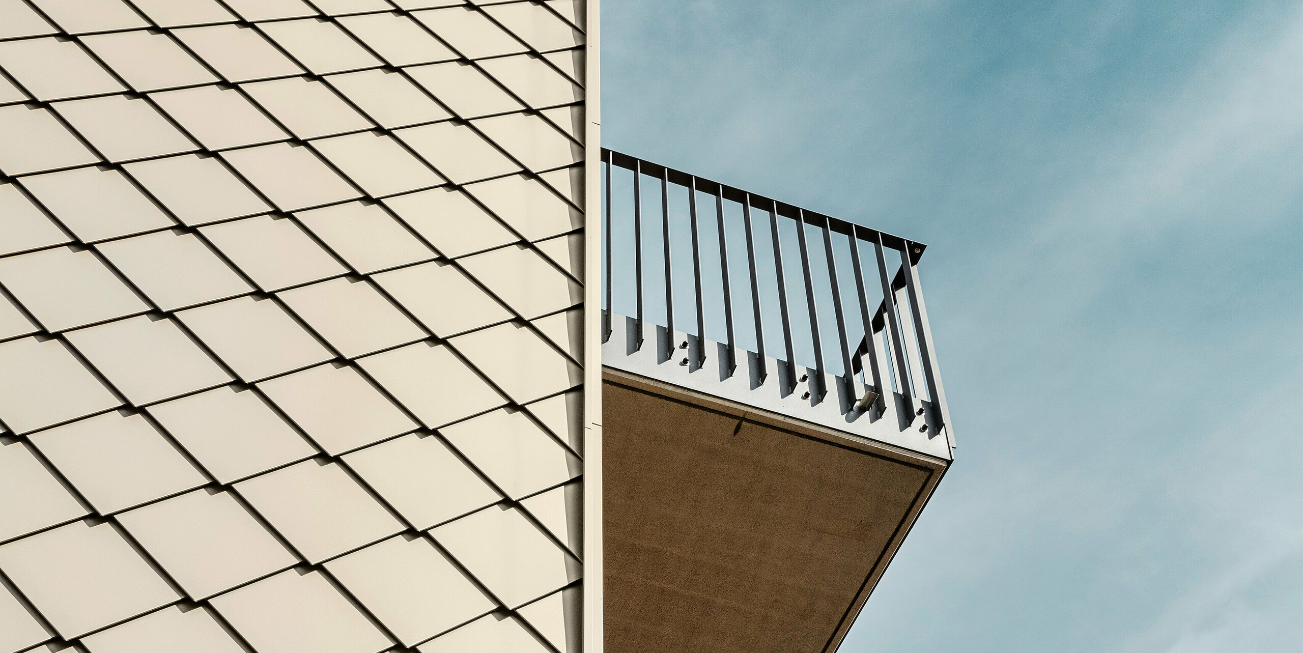 Gros plan de la façade d'une résidence moderne à Dresde avec des losanges de façade PREFA 29 × 29 en bronze disposés avec précision. L'image montre la structure claire de la façade en aluminium de haute qualité ainsi que les balcons avec leurs garde-corps minimalistes qui contrastent avec la surface de couleur bronze. La combinaison des matériaux et des formes souligne l'architecture élégante du bâtiment.