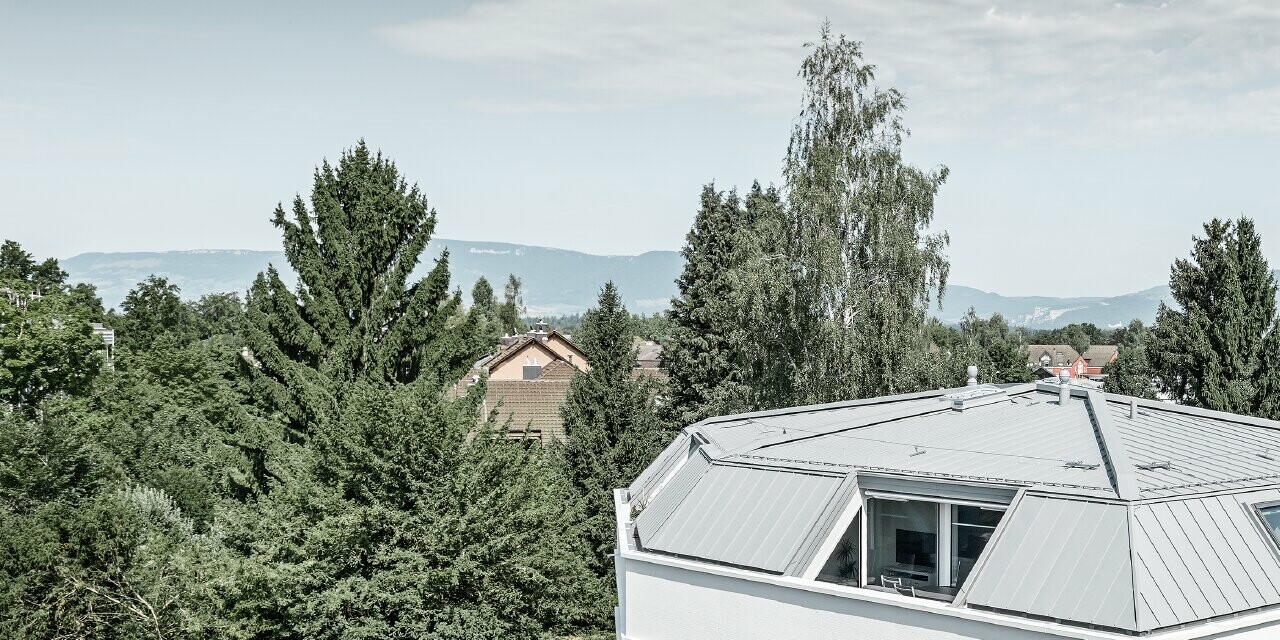 Immeuble collectif épuré avec Prefalz PREFA couleur gris quartz ; La façade est crépie en blanc avec de grandes loggias du côté de l’angle sortant.