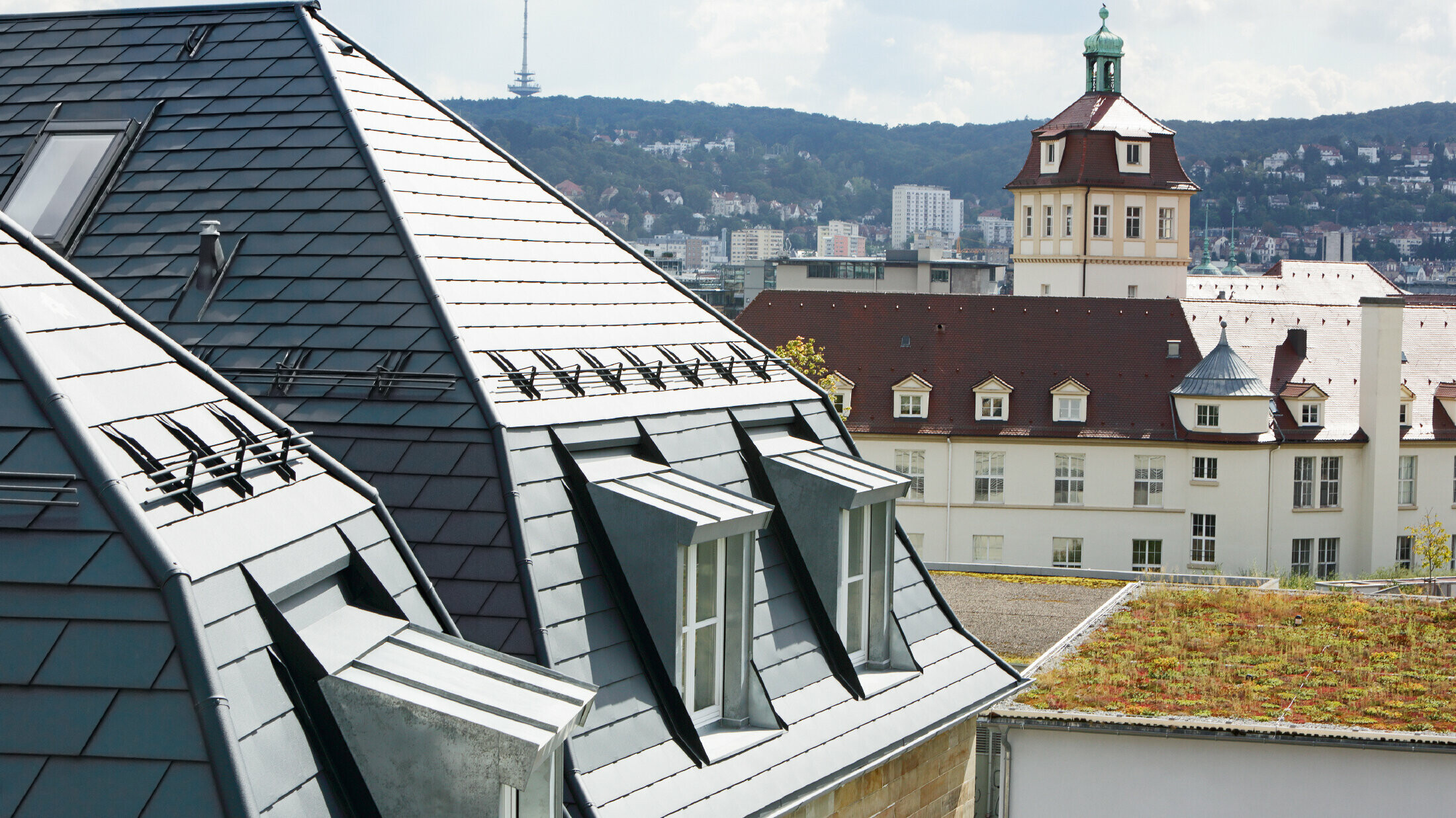 Oud stadshuis in Stuttgart met geknikt dak en veel dakkapellen, bedekt met de aluminium schindels van PREFA in P.10 antraciet