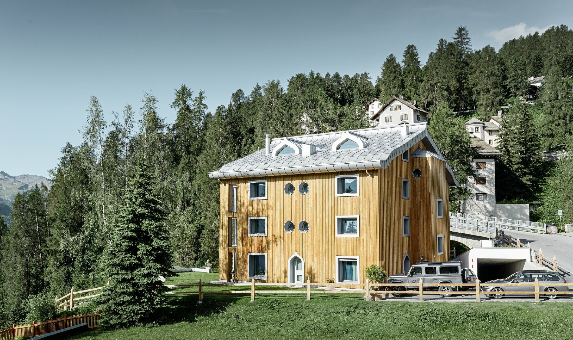 Meergezinswoning in Sankt Moritz (Zwitserland) met houten gevel en aluminiumdak met gekromde dakrand in zilver metallic