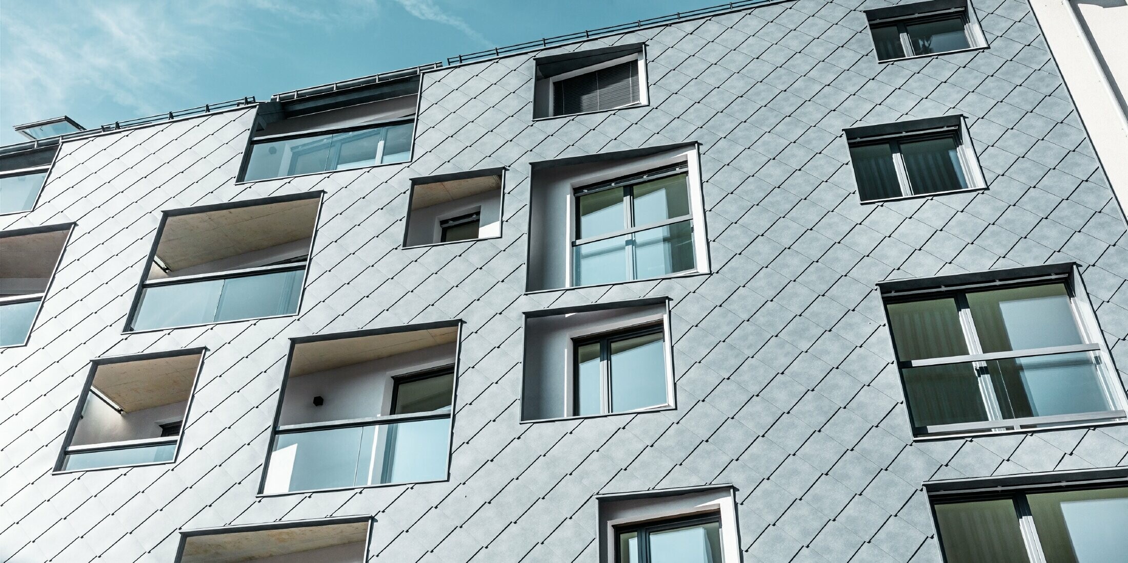 Von unten nach oben fotografiert mit Blick auf die Fassade. Die Sonne strahlt von rechts in das Bild hinein.