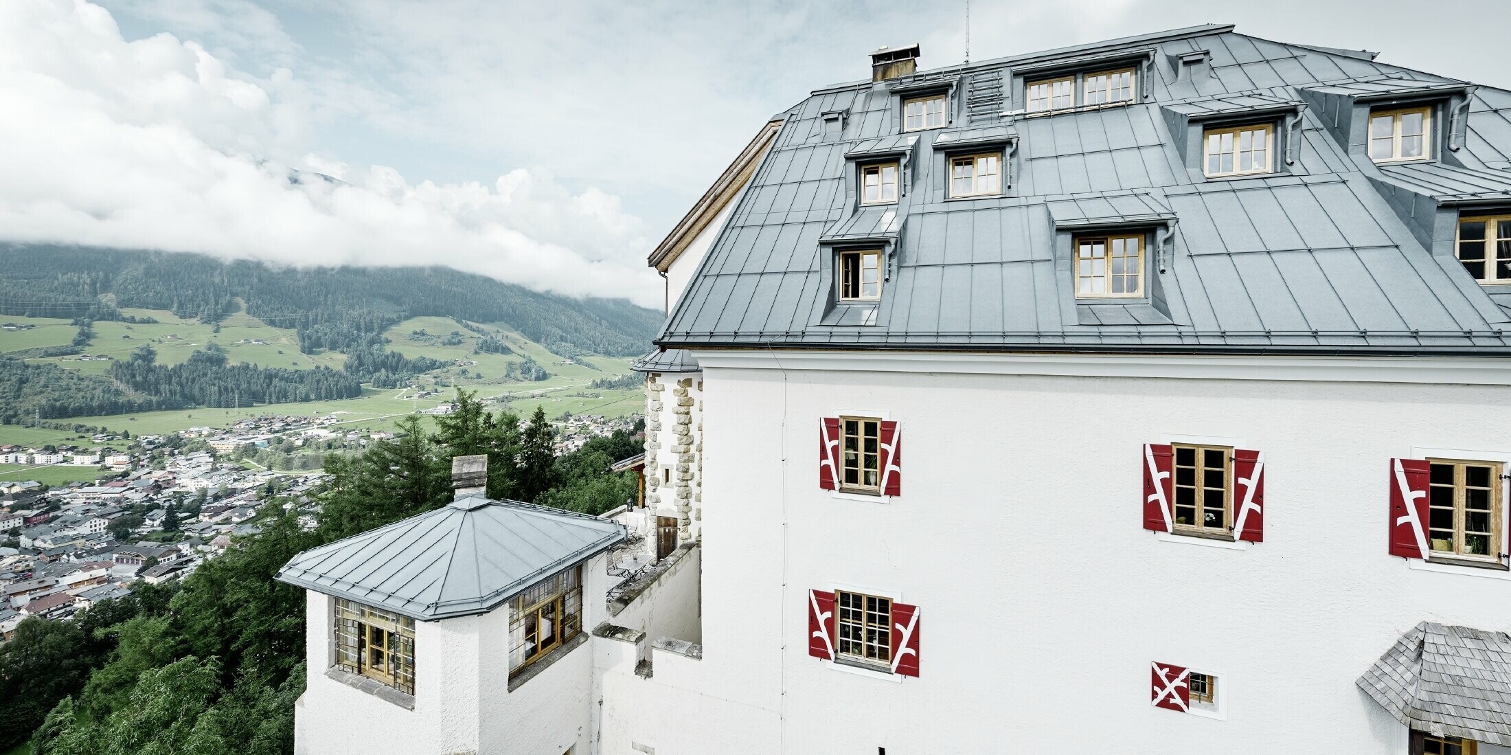 Schloss Mittersill umgeben von Bäumen und Bergen mit einem neu sanierten Prefalz Dach in steingrau