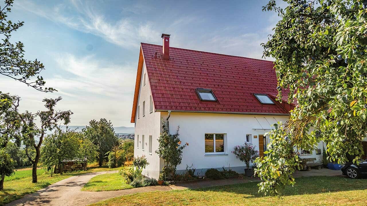 Maisonnette romantique à la campagne avec de nombreux arbres et arbustes. Recouverte avec une toiture PREFA couleur rouge oxyde.