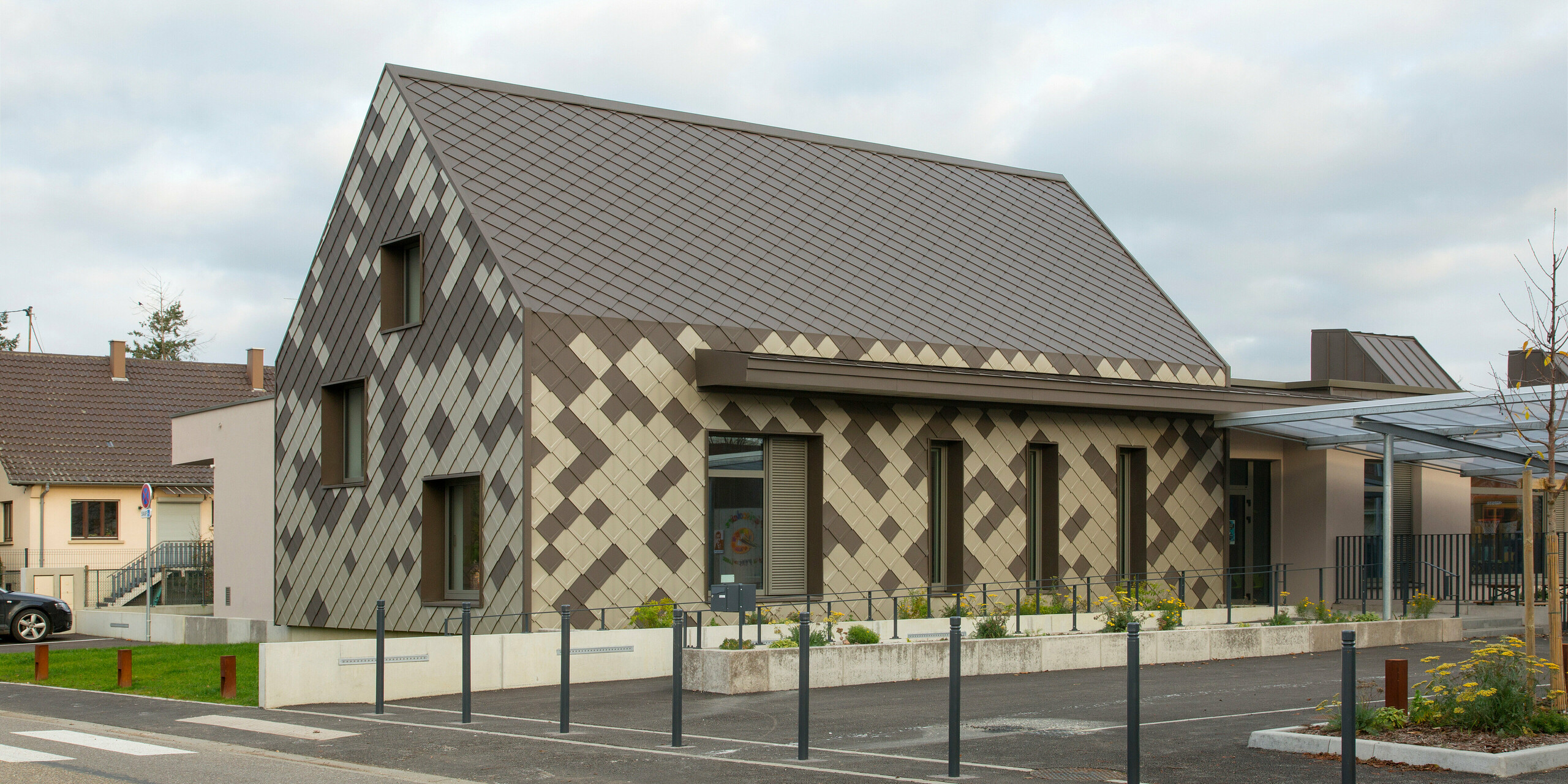 Vue oblique de la garderie périscolaire de Sessenheim. Le bâtiment présente une remarquable coque en aluminium dans les couleurs brun et bronze.