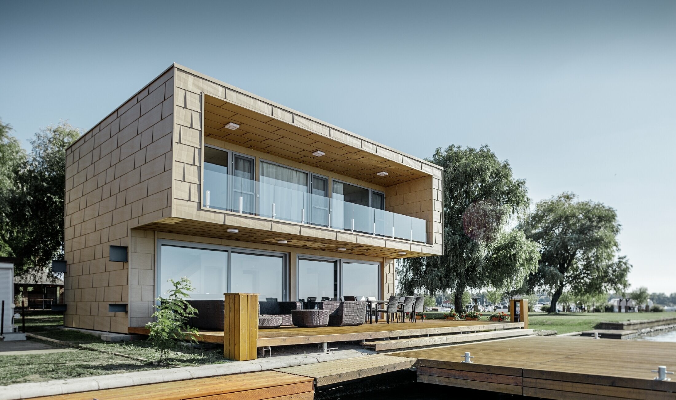 Modern weekendhuis aan het water met plat dak, grote glaspartijen en strakke aluminiumgevel in zandbruin