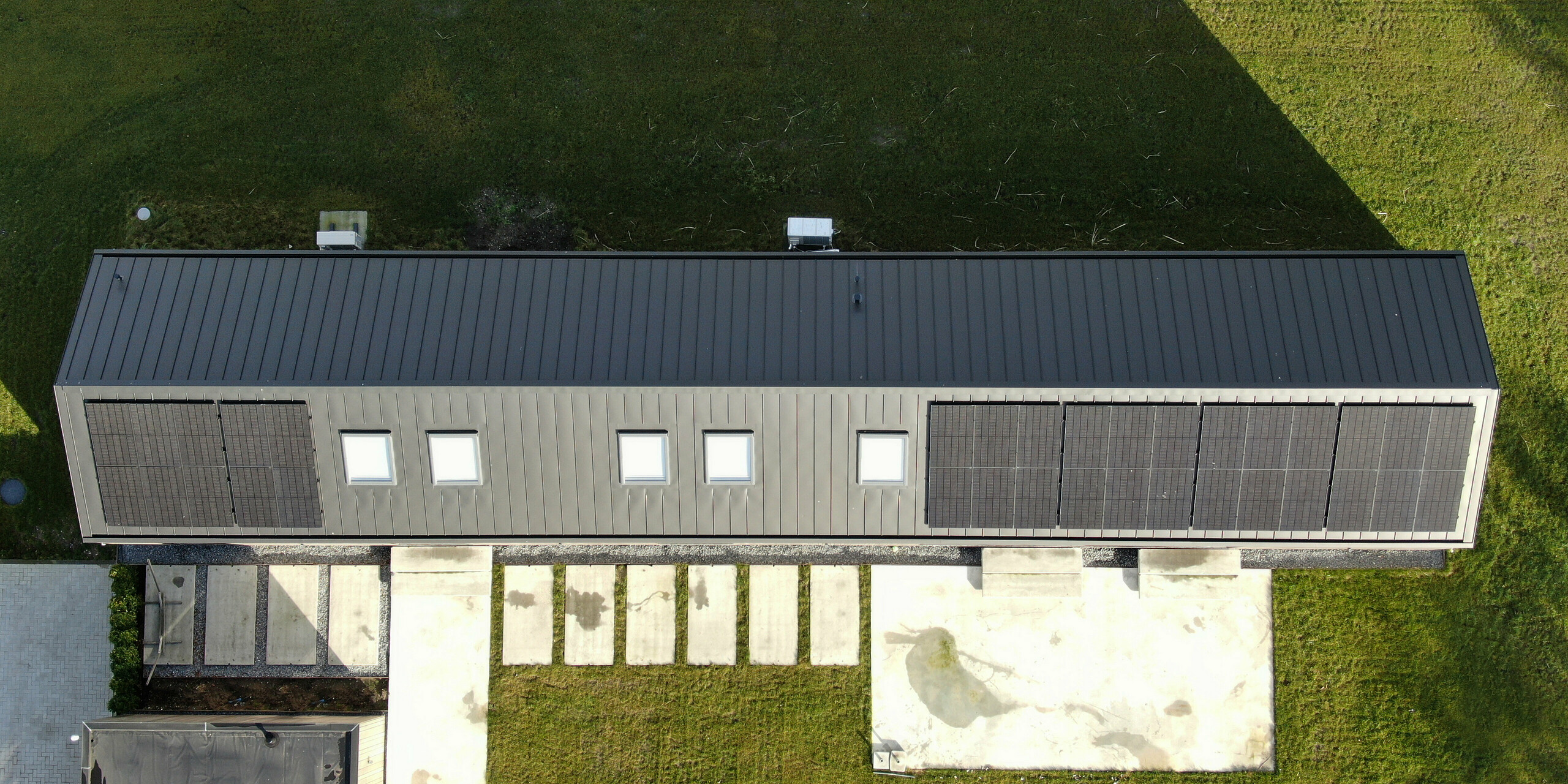 Vue grand angle d'une maison familiale moderne à Uithoorn, aux Pays-Bas, avec toiture à joints debout PREFALZ en gris noir et système photovoltaïque intégré. L'image montre l'utilisation efficace du toit pour les modules solaires ainsi que la construction robuste et résistante aux intempéries du toit en aluminium de haute qualité. Idéal pour les projets de construction durable intégrant les énergies renouvelables et un design moderne.