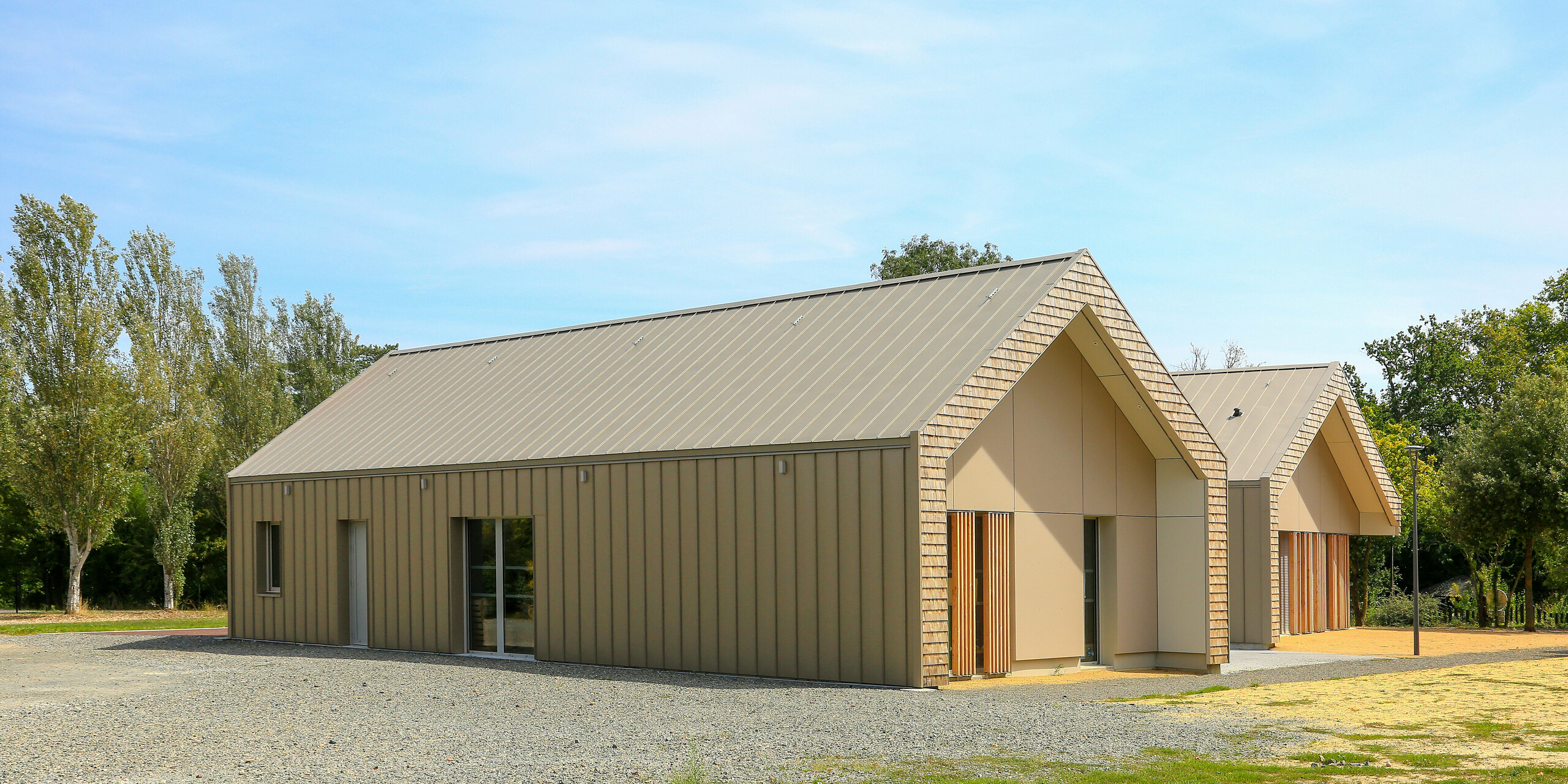 Maison de jeunesse moderne à Mûrs-Erigné, France, avec toiture PREFALZ durable et revêtement de façade en bronze. La toiture en aluminium à joint debout de PREFA impressionne par sa grande résistance aux intempéries et son aspect élégant - idéale pour les projets de construction durables et nécessitant peu d'entretien. La palette de couleurs élégante montre une intégration parfaite dans l'environnement.