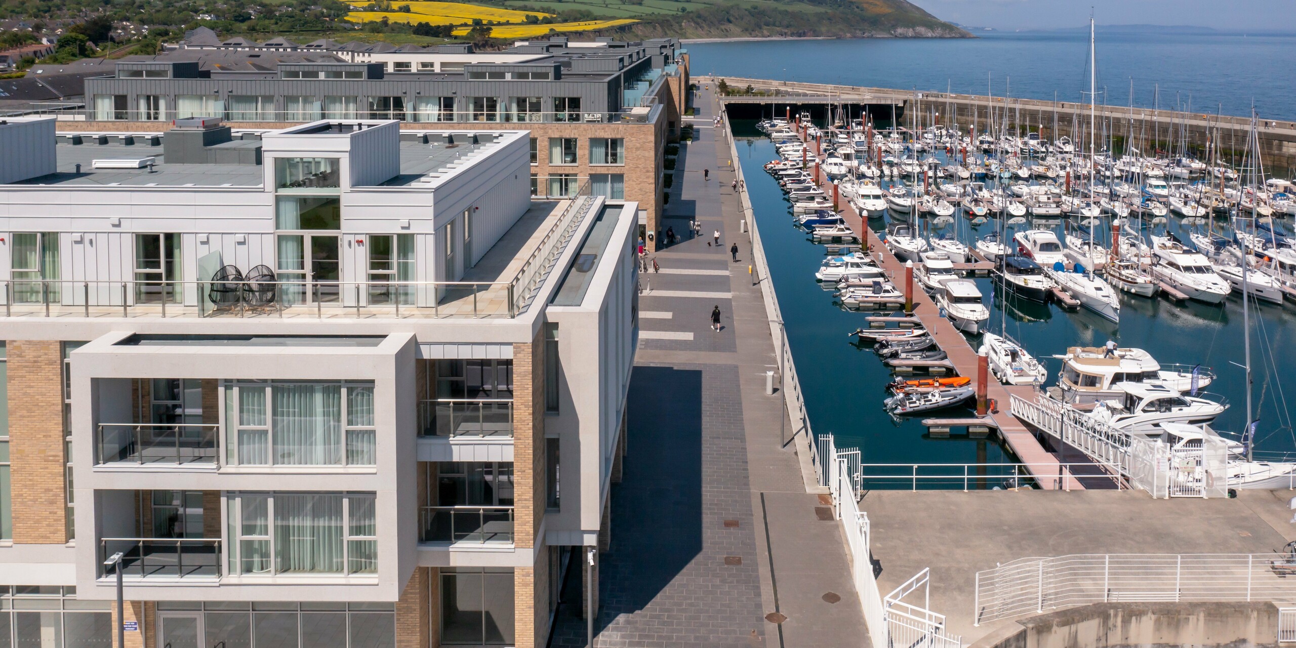 Vue aérienne de Marina Village Greystones à Wicklow, Irlande - Développement résidentiel moderne avec un emplacement direct sur la marina. La façade du complexe résidentiel est conçue avec environ 2 000 m² de PREFALZ robuste dans les couleurs P.10 Prefa blanc et P.10 gris souris. Architecture élégante avec de grandes façades vitrées et balcons, entourée d'un paysage pittoresque au bord de l'eau. Le revêtement en aluminium de haute qualité de PREFA offre une protection durable et une esthétique intemporelle.