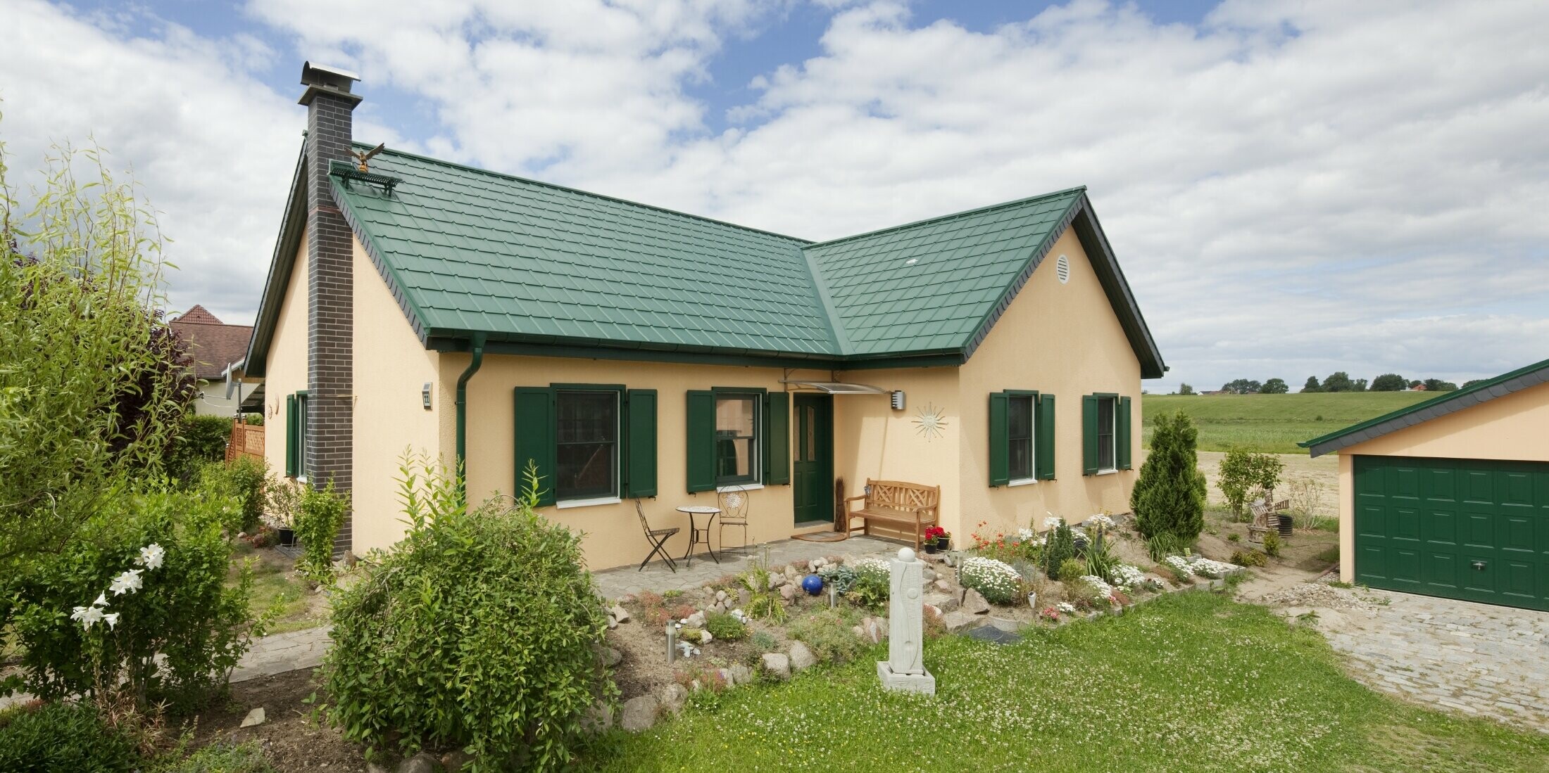erweitertes Satteldach; Satteldach in L-Form; mit der PREFA Dachplatte in P.10 Moosgrün; hübsches ländliches Häuschen mit zum PREFA Dach passenden grünen Fensterläden.
