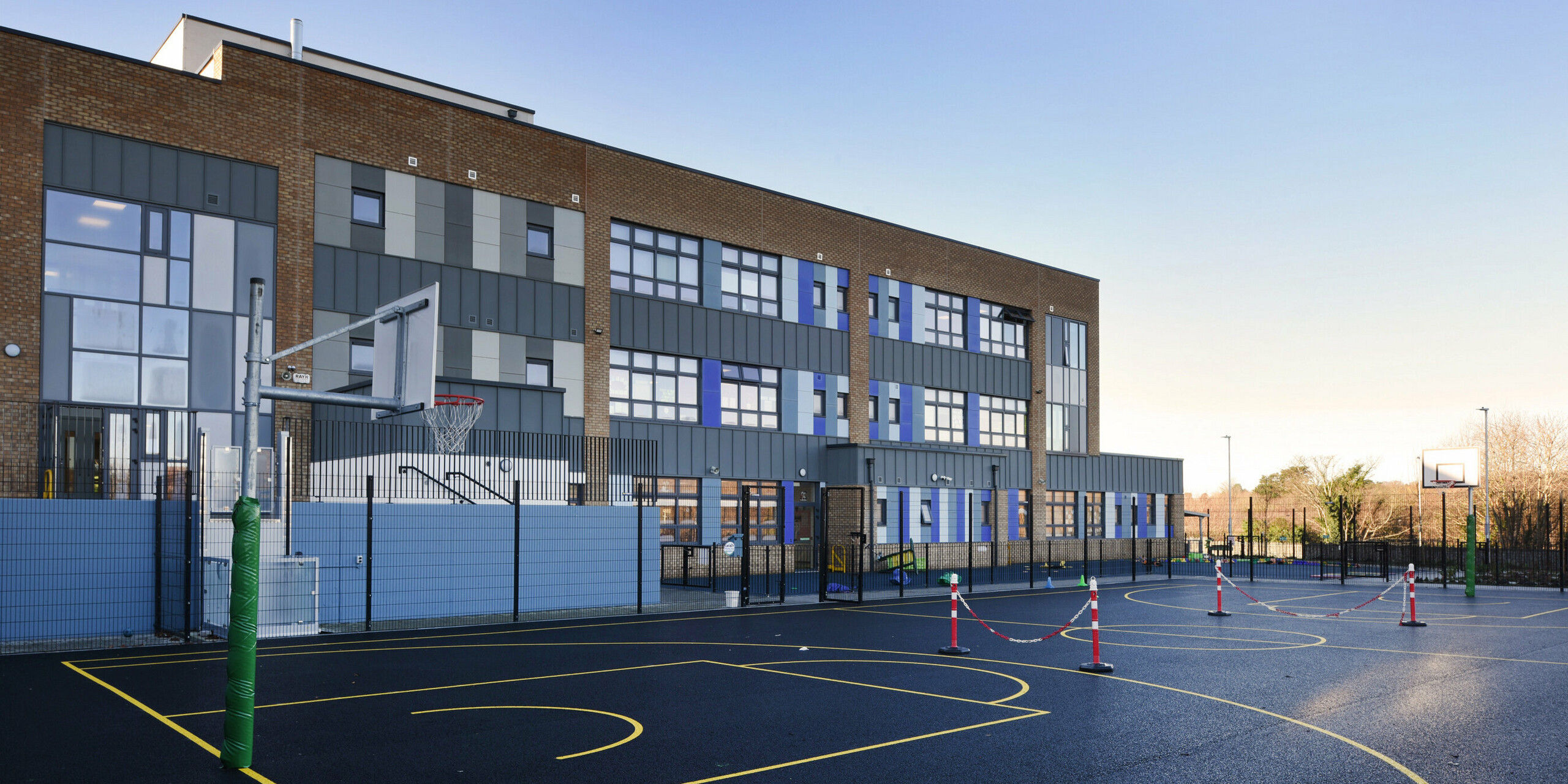 Arrière de l'école nationale Pelletstown Educate Together à Dublin, regardant vers le terrain de basket-ball. Le revêtement en aluminium P.10 gris souris en PREFALZ complète la façade en briques de l'école et offre une protection résistante aux intempéries et un design moderne.