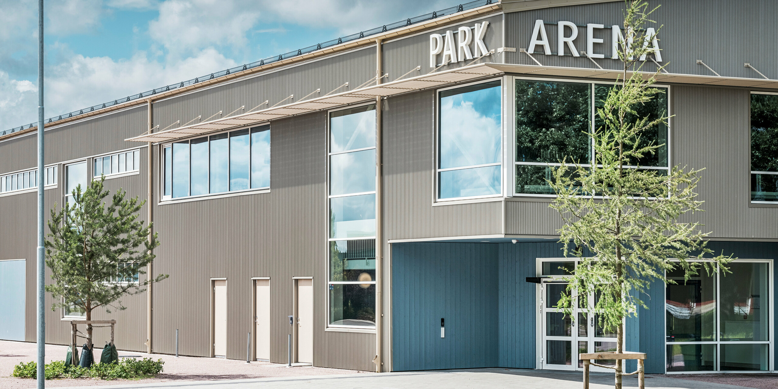 Zone d'entrée du Park Arena de Värnamo, en Suède, avec un design de façade moderne sous la forme du profil extrudé triangle PREFA en bronze. La façade en aluminium durable et résistante aux intempéries confère à la salle de sport de 3 300 m² un aspect élégant et saisissant. Le profil dentelé PREFA crée des effets d'ombre et de lumière fascinants qui mettent en valeur la conception architecturale de l'arène.