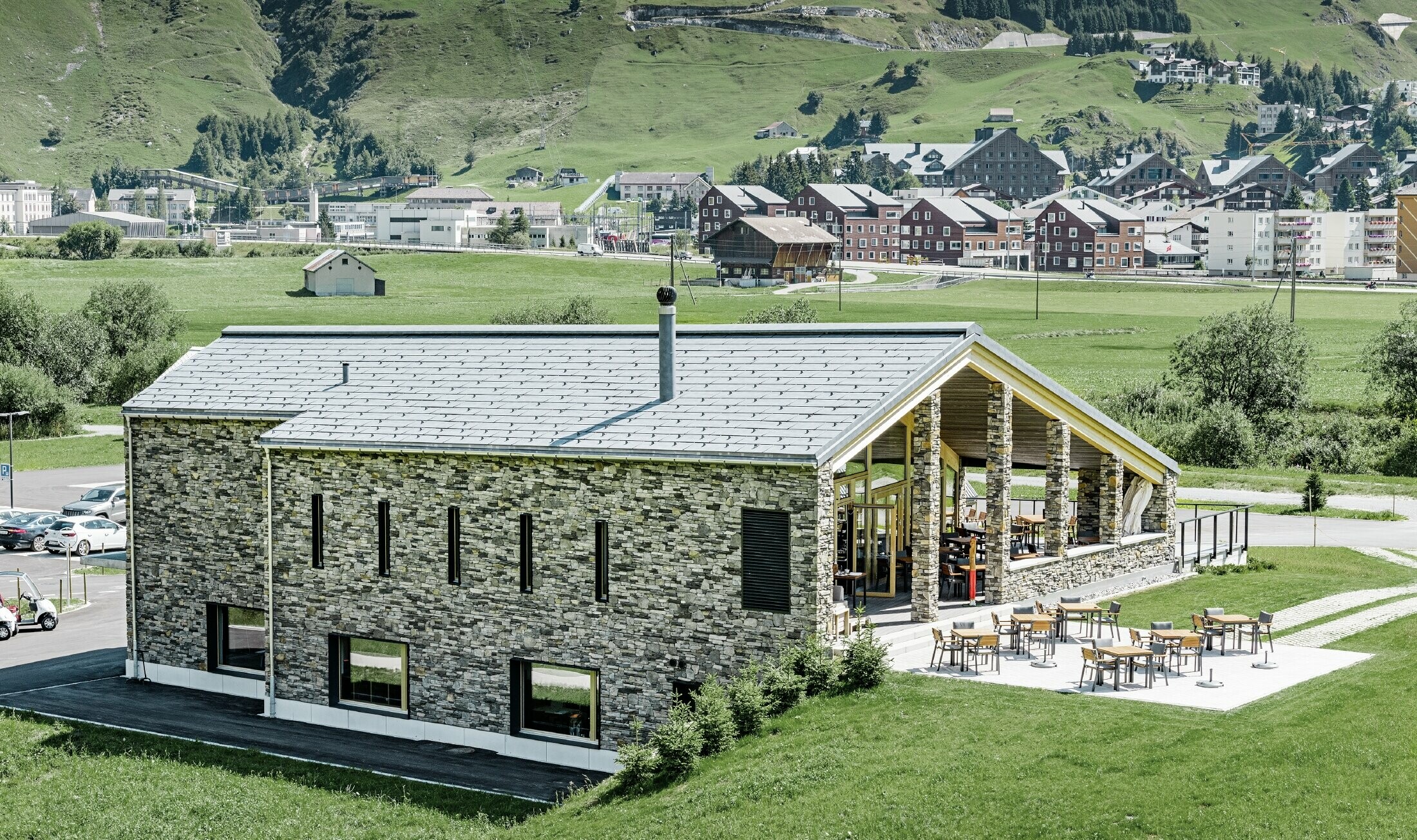 Modern clubhuis van golfterrein in Andermatt (Zwitserland) met gevel in natuursteen en aluminium FX.12 dakpanelen in steengrijs van PREFA 