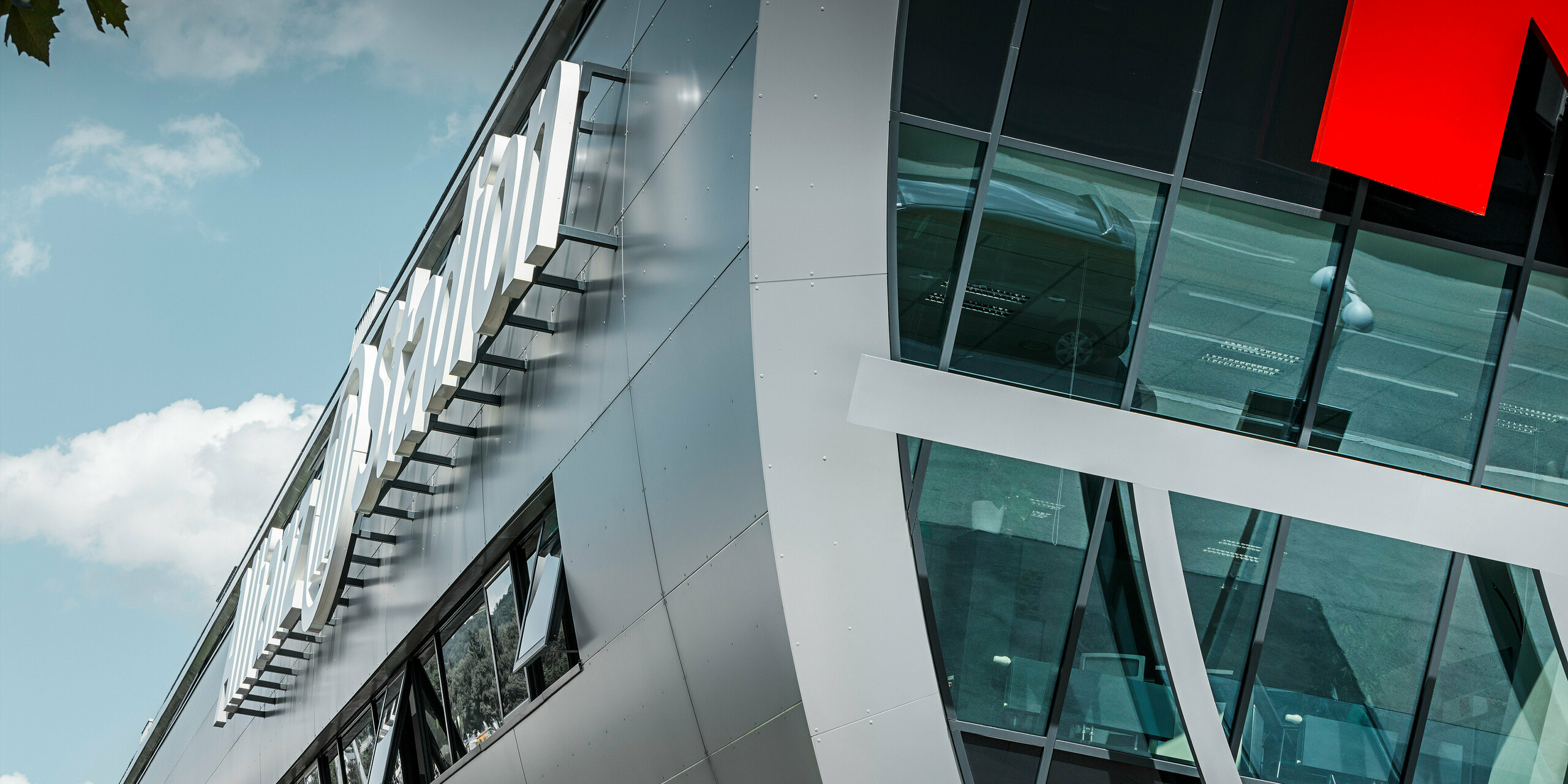 Detailaufnahme der Fassadenverkleidung des Allianz Stadions, der Heimstätte des SK Rapid Wien. Der Fokus des Bildes richtet sich auf die glänzende Fassade aus PREFA Aluminium Verbundplatten in Silbermetallic. Am Bildrand sind der Name des Bauwerks „Allianz Stadion“ sowie die großen Glasflächen und ein Ansatz des leuchtend roten Logos von Rapid Wien zu erkennen.