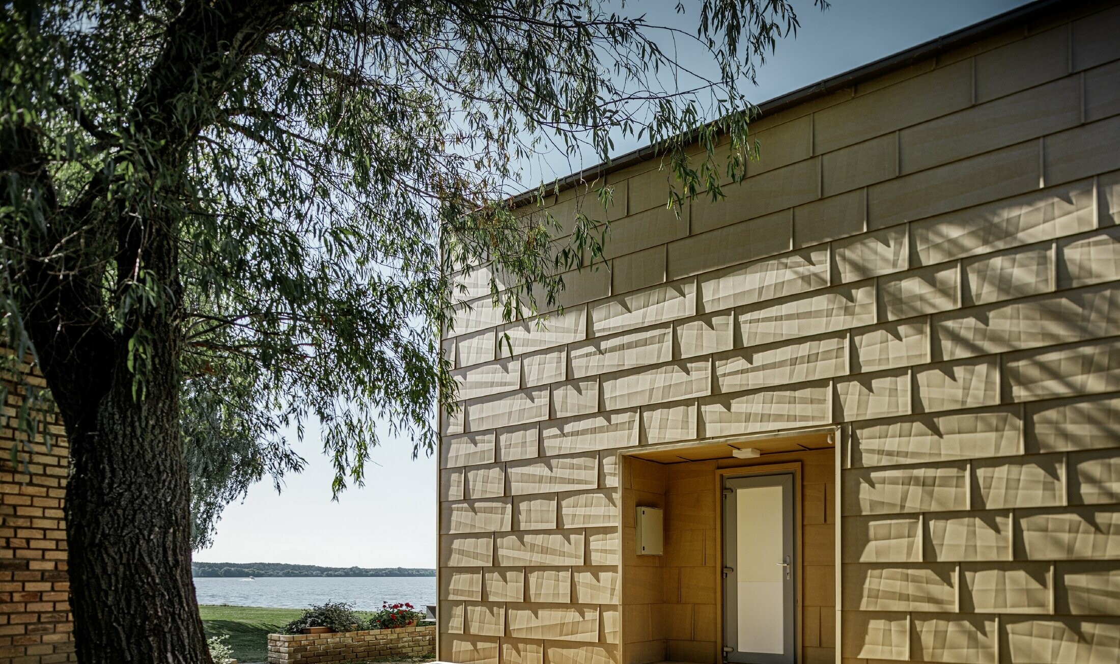 Modern weekendhuis aan het water met plat dak, grote glaspartijen en strakke aluminiumgevel in zandbruin