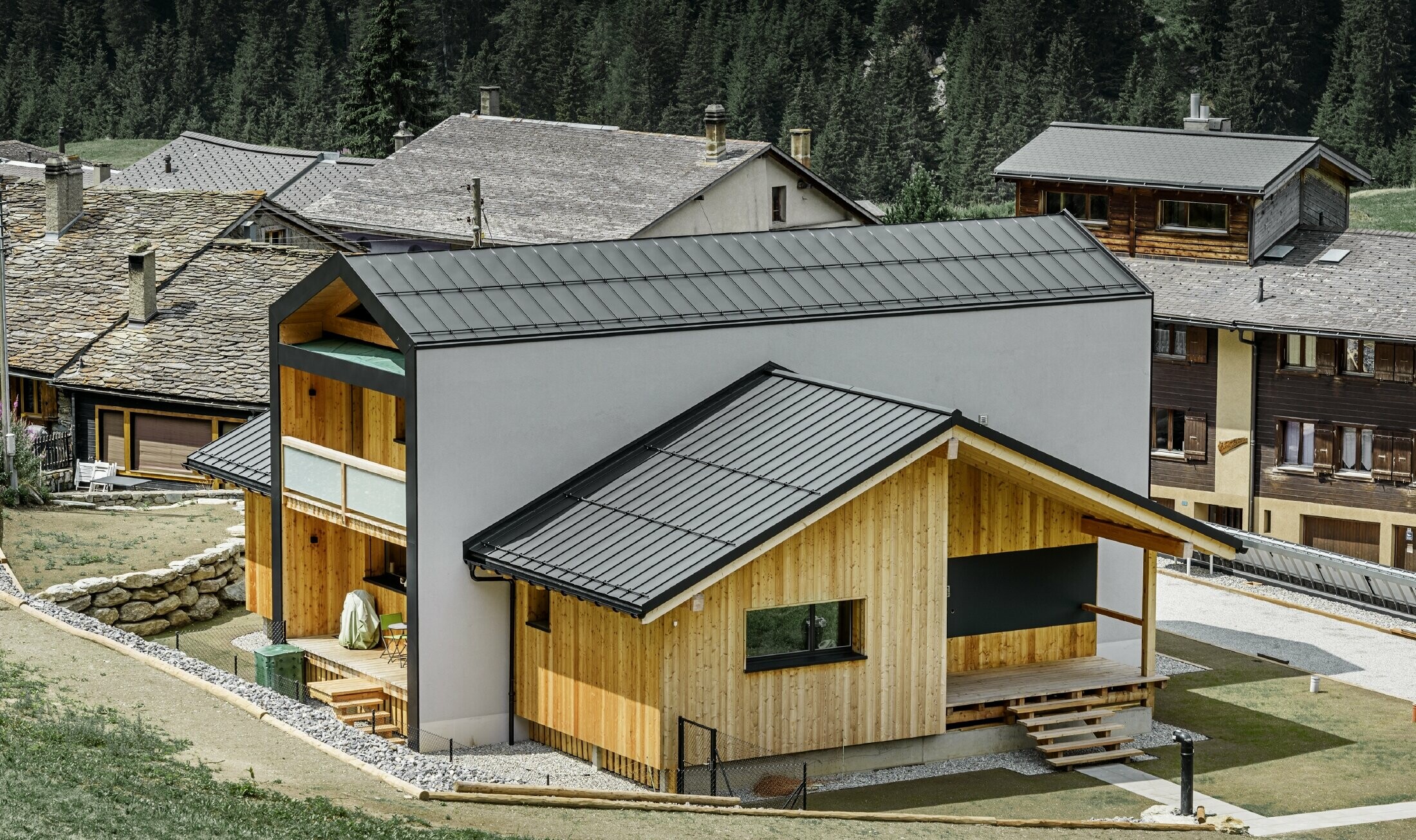 Dieses Einfamilienhaus wirkt, als wären 2 Häuser im 90° Winkel übereinander gestellt worden. Das Dach ist mit Prefalz in Schwarz und die Fassade zum Teil mit Holz verkleidet.