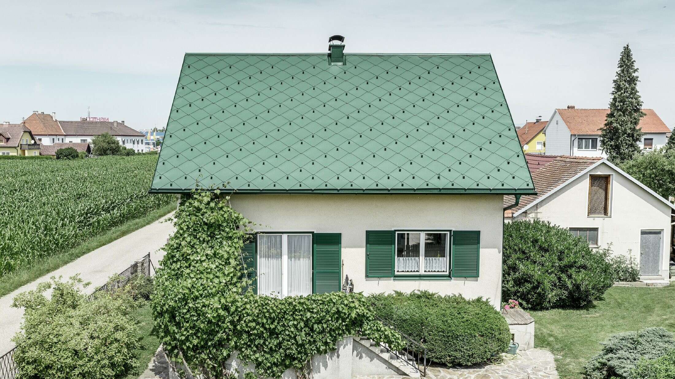 Klassieke eengezinswoning met zadeldak met een dakbedekking van aluminium in mosgroen met groene luiken. Het dak is bedekt met PREFA daklosanges van 44 × 44 in P.10 mosgroen.