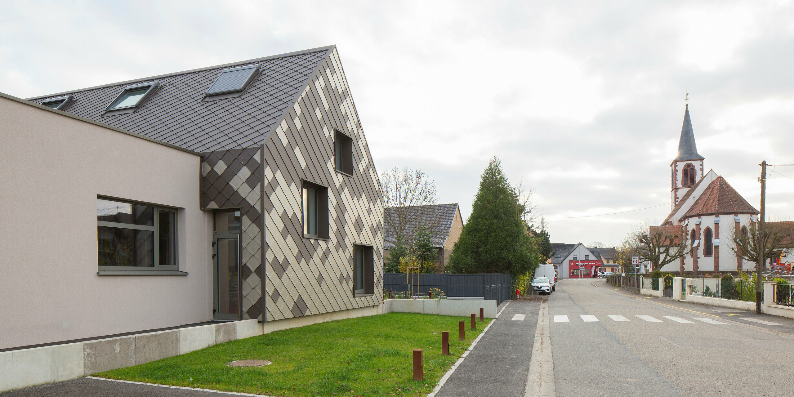 Une rue de Sessenheim : à gauche le périscolaire avec sa coque en aluminium aux couleurs vives, à droite une église.