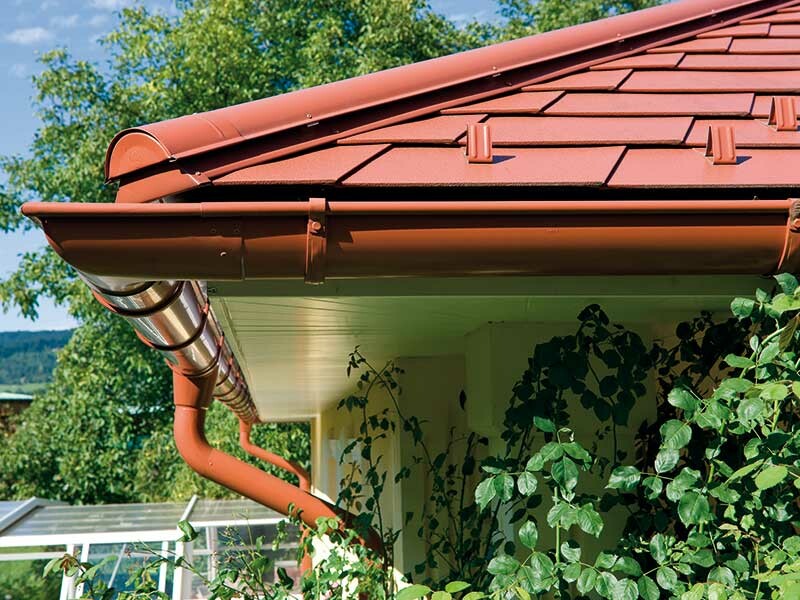 Detailfoto van de PREFA-dakschindel in de kleur baksteenrood en een bijpassende dakgoot, eveneens in baksteenrood.