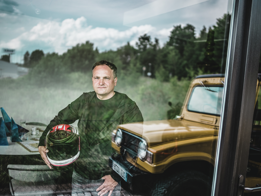 Ein Portrait des Architekten Daniel Zerzan. In der Hand hält er einen Motorradhelm, auch ein gelber Pick-Up ist zu sehen.