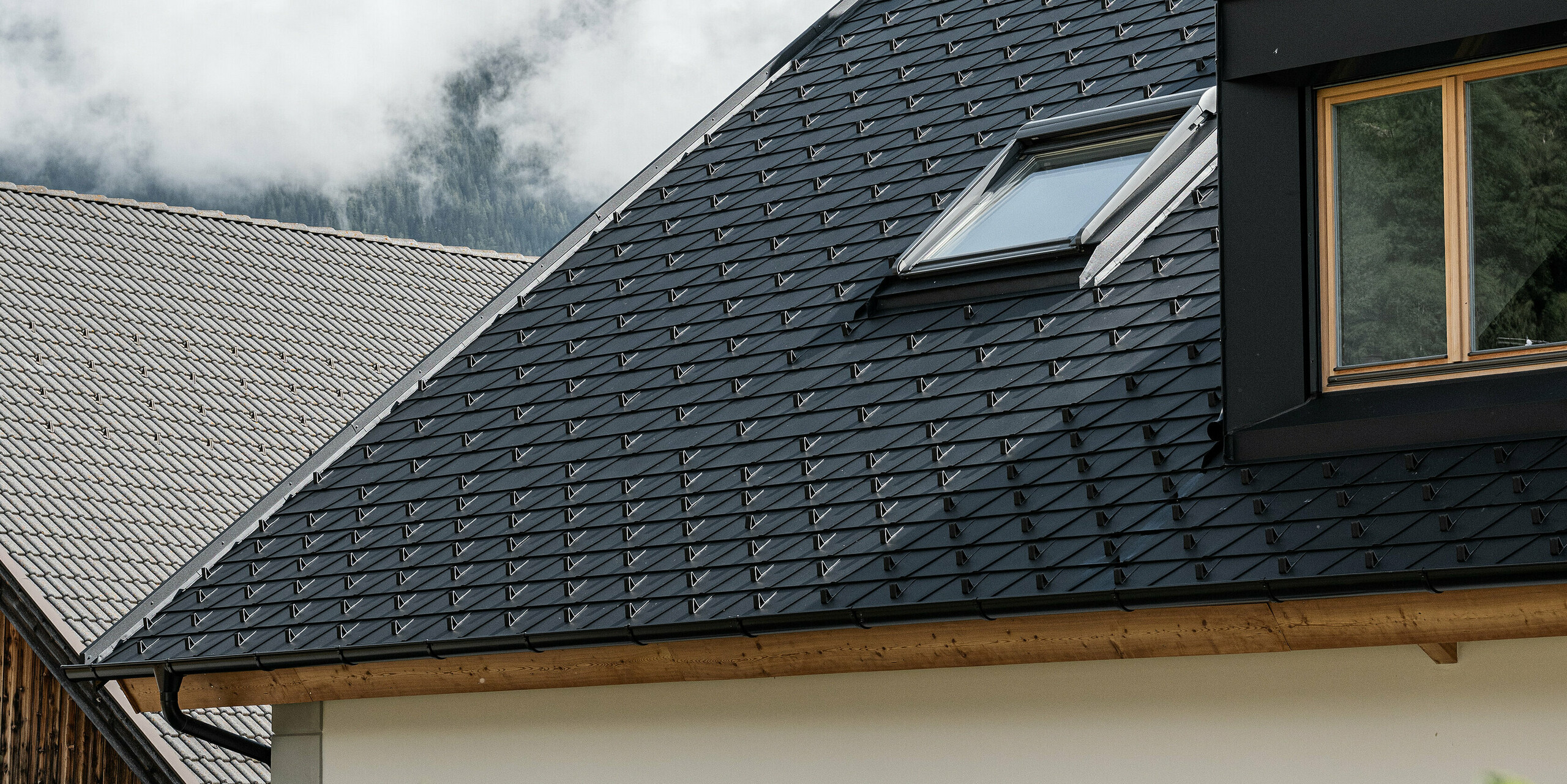 Detailansicht des wind- und wetterfesten PREFA Dachsystems. Das Satteldach des Außerwegerhofs in Südtirol wurde mit robusten PREAF DS.19 Dachschindeln in P.10 anthrazit eingedeckt. Die ästhetische Dachgestaltung ist umgeben von der beeindruckenden Bergkulisse des Antholzertals.