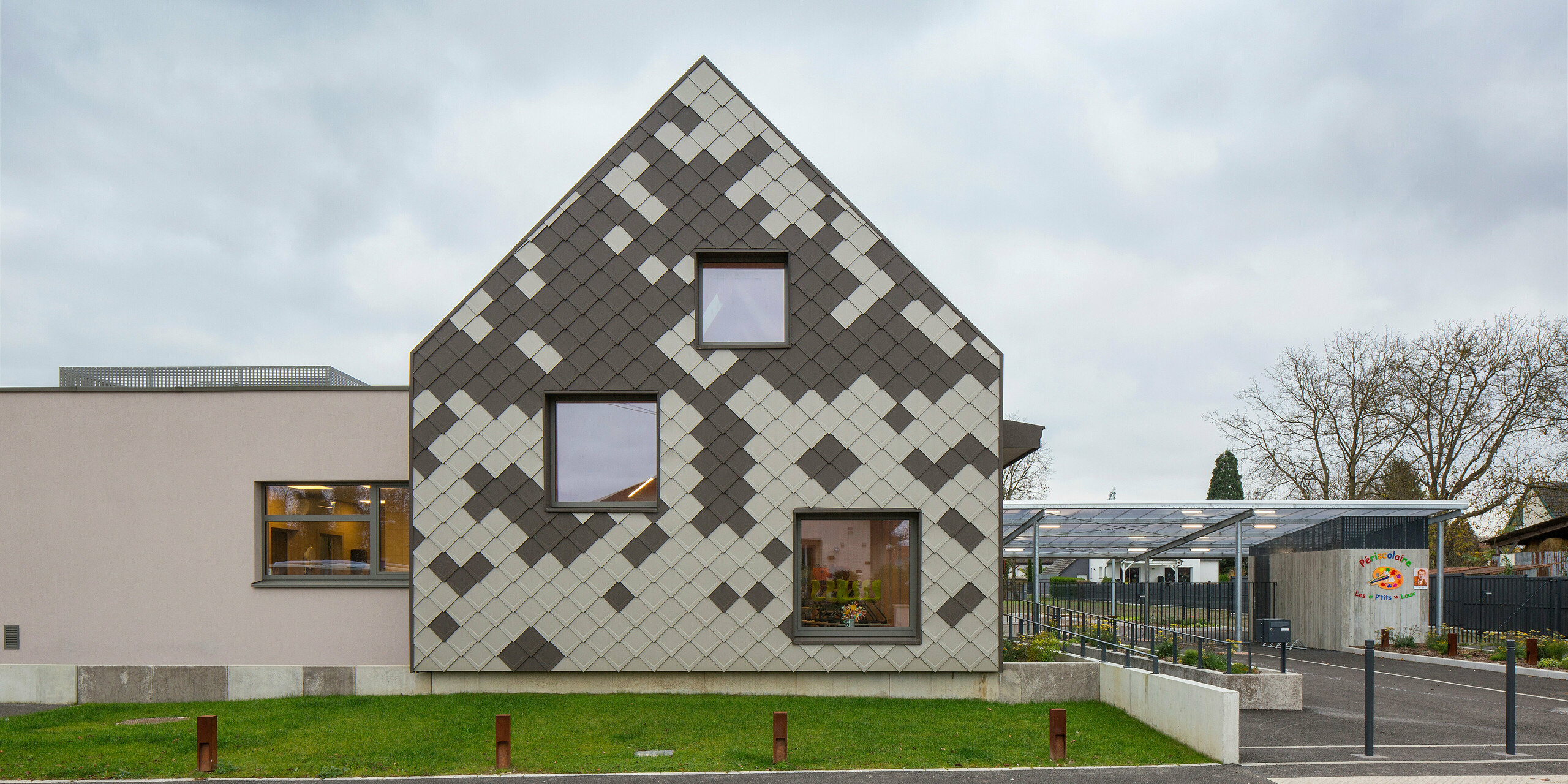 Vue frontale du périscolaire à Sessenheim avec une enveloppe de bâtiment frappante en losanges de toiture et de façade PREFA 29 × 29 dans les couleurs P.10 brun et bronze