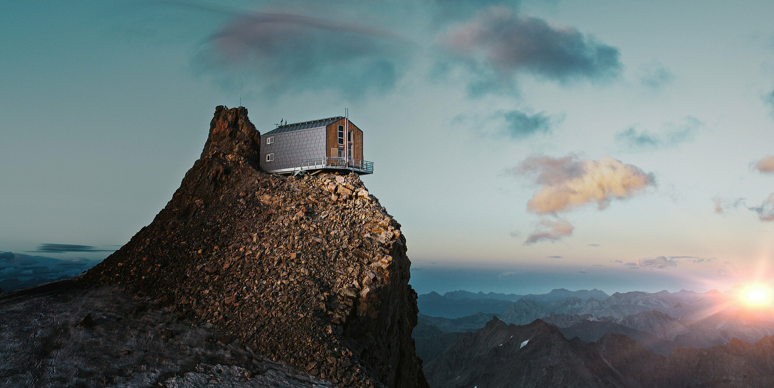 Refuge de l'Aigle auf 3.450 Meter über dem Meeresspiegel. Die Berghütte thront bei Sonnenuntergang auf einem Gipfel in La Grave, Frankreich, mit PREFA Dach- und Fassadenpaneelen FX.12 in Steingrau.