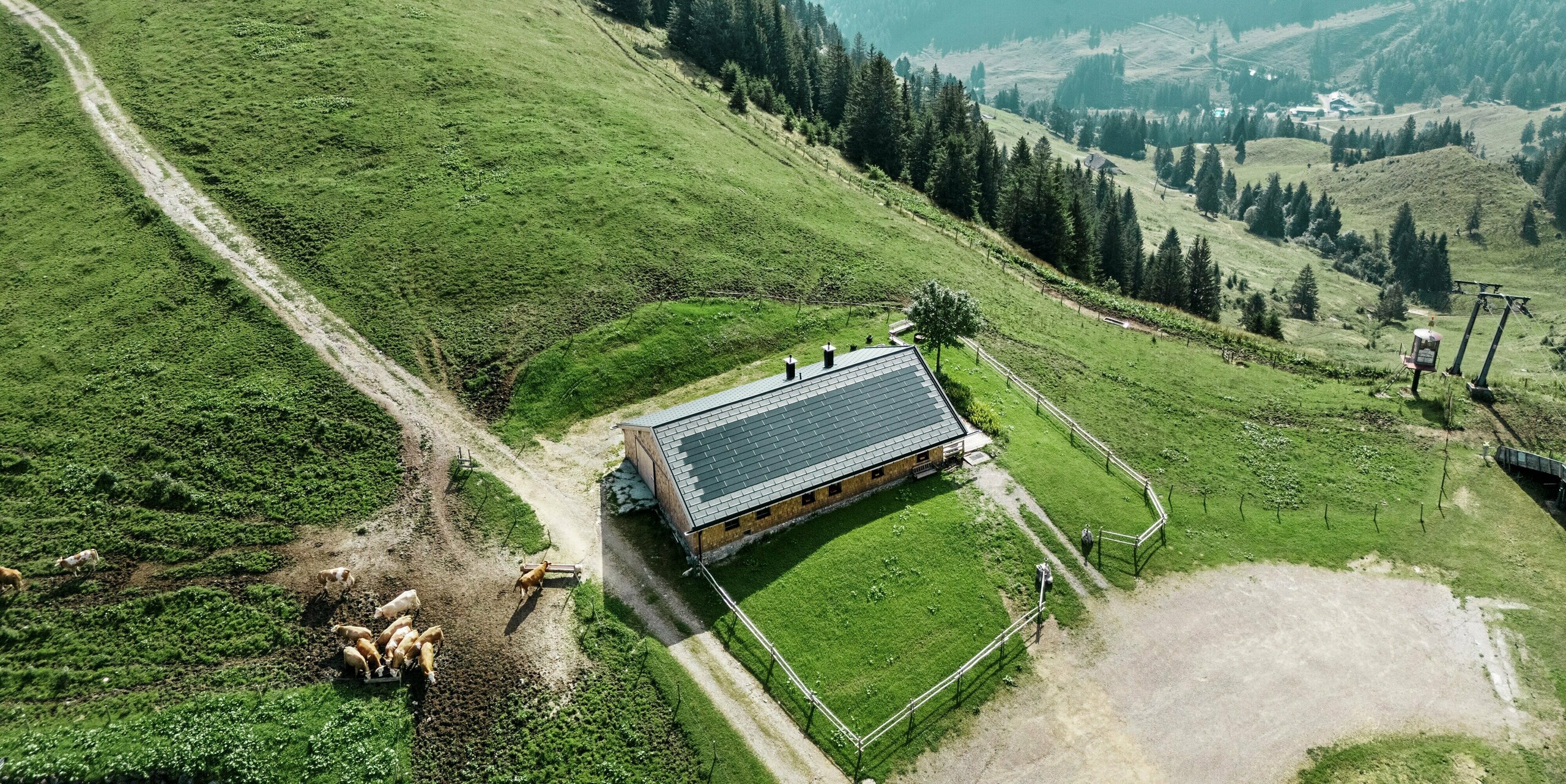 Prise de vue par drone de la Birkehütte sur le Walleralm à Bayrischzell au milieu d'un paysage de montagne idyllique. Lors de la rénovation, le toit a été équipé de panneaux de toiture durables PREFA R.16 en noir P.10 et de tuiles solaires innovantes PREFA. Cette solution moderne associe la production d’énergie durable à la protection robuste des produits en aluminium PREFA éprouvés et s’intègre harmonieusement dans l’environnement alpin.