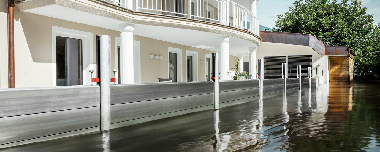 Zu sehen ist ein Einfamilienhaus mit Balkon. Durch den PREFA Hochwasserschutz ist das Haus vor dem bereits steigenden Hochwasser geschützt.