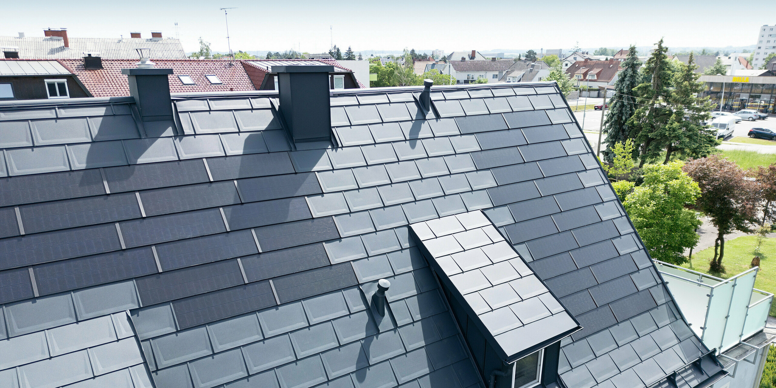 Toiture entièrement rénovée d'une maison familiale à Leonding avec des tuiles solaires PREFA en anthracite. Le gros plan montre le toit en aluminium modernisé avec des modules solaires intégrés de PREFA. Cette solution durable et résistante aux intempéries offre un moyen durable et économe en énergie de produire de l’électricité. L'image illustre l'intégration esthétique des modules solaires dans la surface du toit, qui soutient une architecture moderne et fonctionnelle. Les longues lucarnes recouvertes de R.16 attirent également l'attention dans l'aménagement du toit.