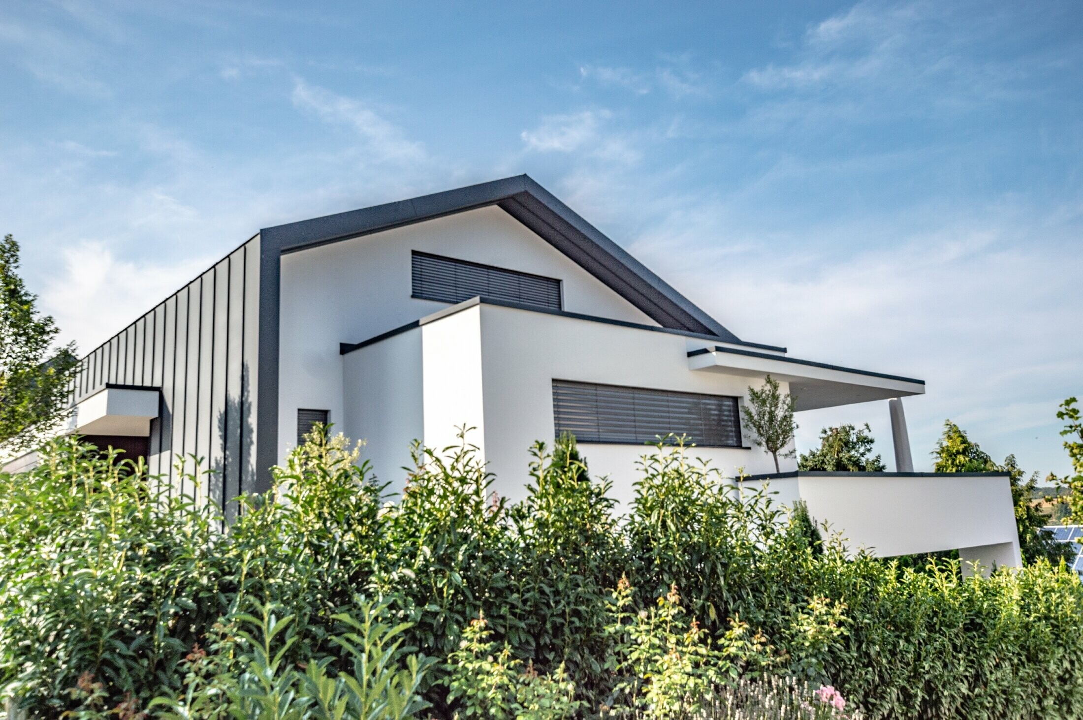 Maison individuelle moderne où la couverture de toit se prolonge sur la façade par agrafage. La couleur du matériau PREFA est l’anthracite.